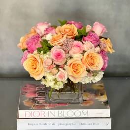 Low arrangement of peach and pink roses in a glass vase set on fashion books