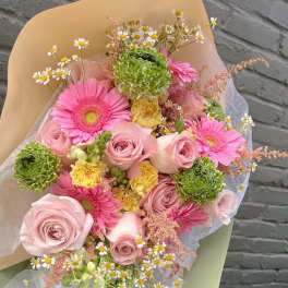 Bouquet of pink roses, gerbera daisies, and green blooms wrapped in paper