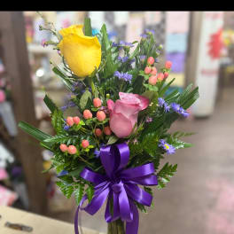 Bouquet of yellow and pink roses in a glass vase with a purple ribbon