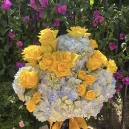 Yellow roses and blue hydrangeas in a dark vase with a yellow ribbon