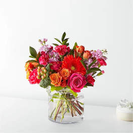 Mixed bouquet of pink, orange, and red flowers in a clear glass vase
