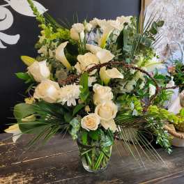 White roses and calla lilies in a glass vase with greenery