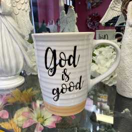White mug with the words "God is good" on display among angel decor