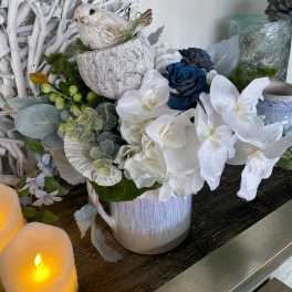 White and blue floral arrangement in a ceramic pot with a bird figurine