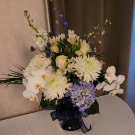 White and lavender floral arrangement in a dark vase with a ribbon