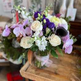 Mixed bouquet with orchids, roses, and purple blooms in a glass vase