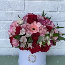 Pink and red flower arrangement in a white hat box