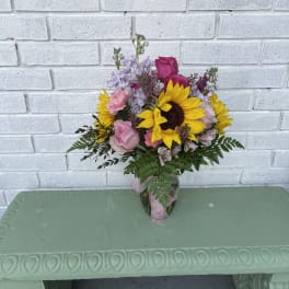 Bouquet of sunflowers, pink roses, and lavender flowers in a glass vase