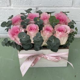 Pink roses arranged in a rectangular box with eucalyptus and a pink ribbon