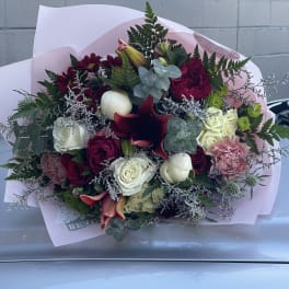 Mixed bouquet of roses, lilies, and carnations wrapped in pink paper