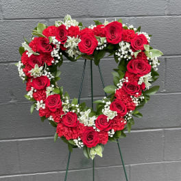 Heart-shaped floral wreath with red roses and white filler flowers on a stand