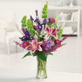 Tall mixed arrangement with pink lilies and purple flowers in a clear glass vase