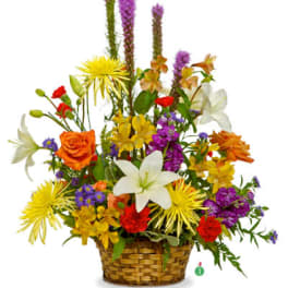Tall mixed arrangement of white lilies, orange roses, and bright blooms in a woven basket.