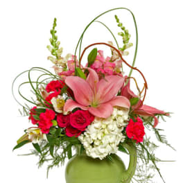 Tall arrangement of pink lilies, red roses and white hydrangeas in a green ceramic pitcher