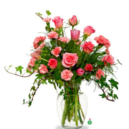 Pink roses, tulips, and carnations arranged in a clear glass vase with trailing ivy