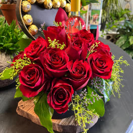 Red roses arranged with a wine bottle and chocolates in a heart-shaped box