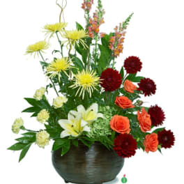 Mixed arrangement with yellow spider mums, lilies, orange roses and dark red blooms in a brown bowl