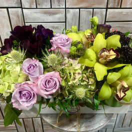 Mixed bouquet with lavender roses and bright green orchids in a white container