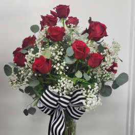 Red roses in a glass vase with white baby's breath and a striped ribbon