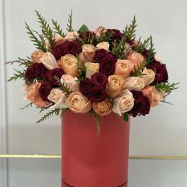 Bouquet of peach and burgundy roses in a red cylindrical vase