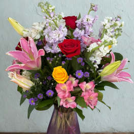 Mixed bouquet of roses, lilies, and purple flowers in a purple vase