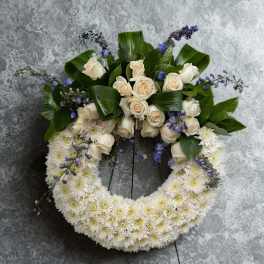 White floral wreath with cream roses and purple accents on a stand