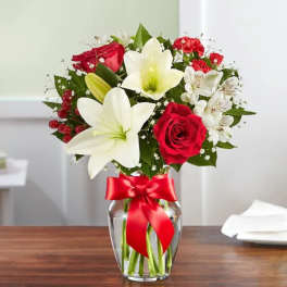 Bouquet of red roses and white lilies in a glass vase with a red ribbon