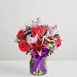 Bouquet of pink roses and lilies in a clear glass vase with a purple ribbon