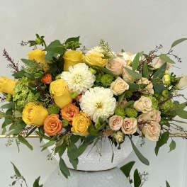 Mixed bouquet of yellow, peach, and white flowers in a white vase