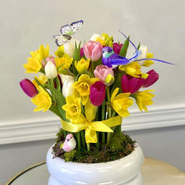 Bright arrangement of yellow daffodils and multicolor tulips in a white pot with decorative birds and butterfly