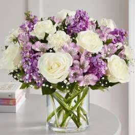 Bouquet of white roses and purple flowers in a clear glass vase