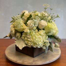 Creamy white floral arrangement in a dark square box on a round marble base