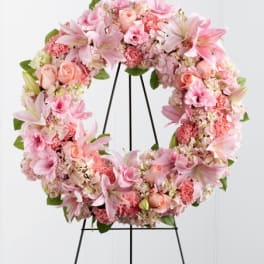 Pink floral wreath on a black stand with lilies and roses
