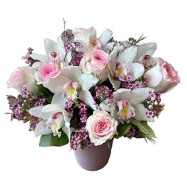 Low arrangement of pink roses, white cymbidium orchids, and tiny purple blooms in a soft pink vase