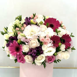 Round bouquet of pink, white, and purple flowers in a pink box