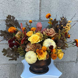 Autumn floral arrangement with yellow roses, marigolds, and small pumpkins in a dark vase