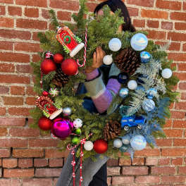 Person holding a decorated Christmas wreath with ornaments and pinecones