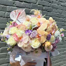 Pastel bouquet with orchids, roses, and a white anthurium in a round box