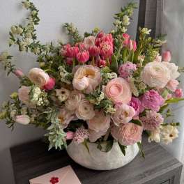Pink and white mixed flower arrangement in a ceramic bowl with a card
