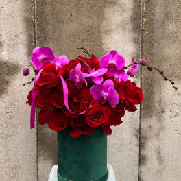 Red roses and pink orchids in a green hatbox