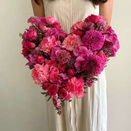 Heart-shaped bouquet of pink flowers held by a person in a white dress