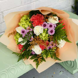 Mixed bouquet of roses, carnations, and purple daisies wrapped in peach paper