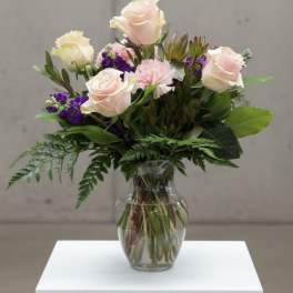 Pink roses and purple flowers arranged in a clear glass vase