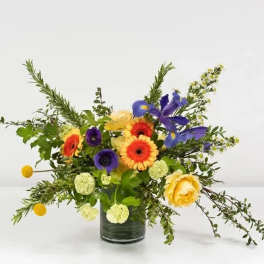 Mixed bouquet in a glass vase with orange, yellow, purple, and blue blooms
