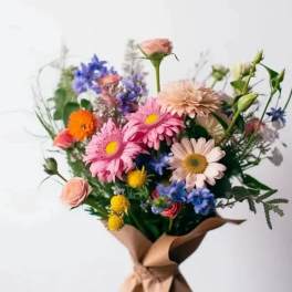 Mixed bouquet of pink, blue, and yellow flowers wrapped in brown paper