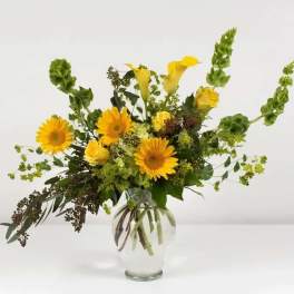 Yellow flowers in a clear glass vase with tall green accents