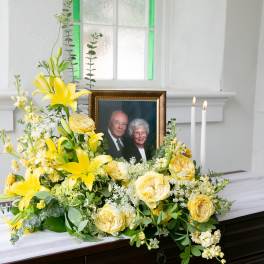 Yellow floral arrangement beside a framed photo and candles on a casket