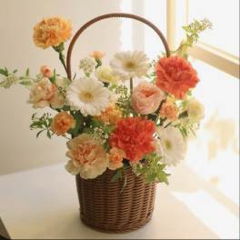Basket arrangement of peach and white flowers with a woven handle