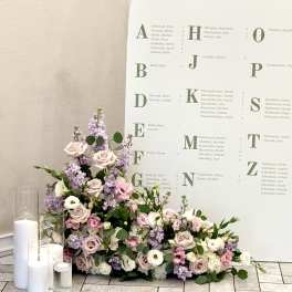 Pastel floral arrangement with roses and lavender blooms beside white candles