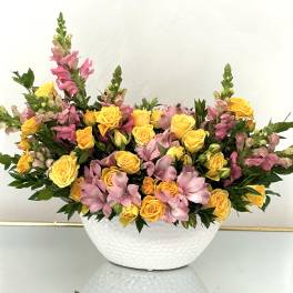 Yellow roses and pink snapdragons arranged in a white bowl vase